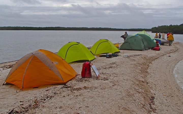 A group of tents rest on a small, sandy peninsula.